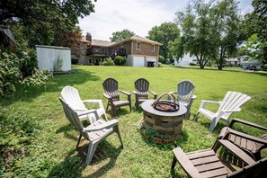 Un jardin avec un foyer, quatre fauteuils Adirondack et une pelouse verdoyante.
