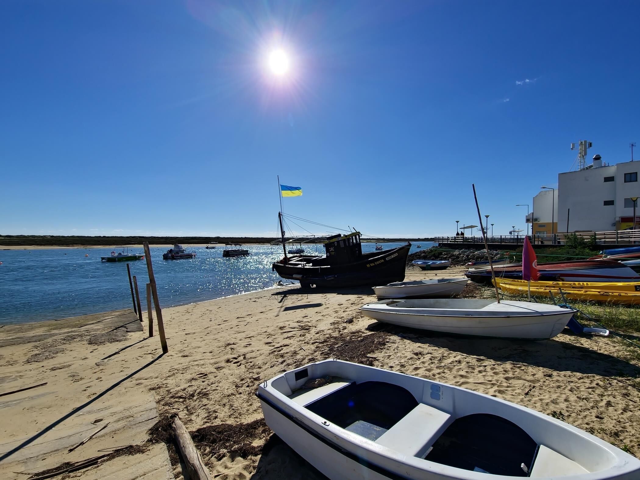 Uma praia com barcos, céu claro e um edifício ao fundo.