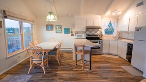 A kitchen with wooden flooring, white cabinets, a dining table with chairs, a microwave, and an oven. - Bayside House - Quiet neighborhood (Harvey Cedars)