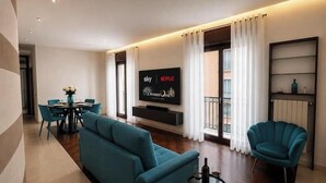 En moderne stue med et fladskærms-tv, turkise sofaer, et spiseområde og en balkon med gardiner.