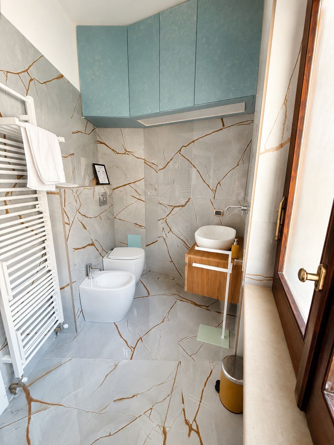 Une salle de bain avec des toilettes blanches, un lavabo, un miroir et un porte-serviettes.