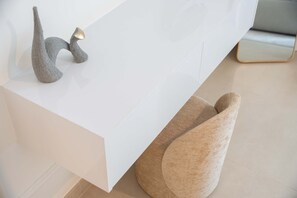 Ein modernes, minimalistisches Zimmer mit einem weißen Empfangstresen, einer strukturierten Skulptur und einem großen, hellen Sessel.
