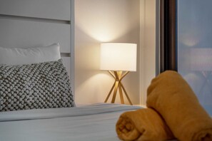 A neatly made bed with a white pillow and a textured pillow, a lamp with a white shade, and a rolled towel on the bed. - PC404A-Pool View-Perfect for family or a group-Close to Palm Beach-3BR (Palm Beach)