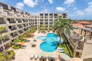 A hotel with a central pool surrounded by sun loungers and palm trees. - PC404A-Pool View-Perfect for family or a group-Close to Palm Beach-3BR (Palm Beach)