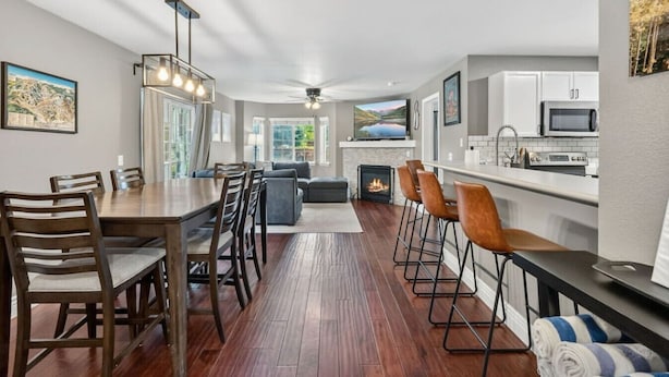 A modern kitchen with a built-in microwave, a dining area with a wooden table and chairs, a fireplace, and a bar area with stools. - Alpine Escape | Pool, Hot Tub & Mountain Access (Edwards)
