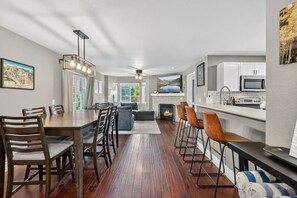 A modern kitchen with a built-in microwave, a dining area with a wooden table and chairs, a fireplace, and a bar area with stools. - Alpine Escape | Pool, Hot Tub & Mountain Access (Edwards)