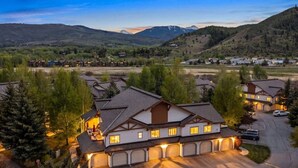 A large, multi-story building with a garage, surrounded by trees and a mountainous landscape. - Alpine Escape | Pool, Hot Tub & Mountain Access (Edwards)