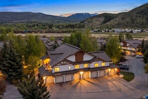 A large, multi-story building with a garage, surrounded by trees and a mountainous landscape. - Alpine Escape | Pool, Hot Tub & Mountain Access (Edwards)