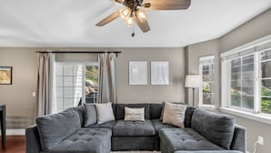 A modern living room with a sectional sofa, a ceiling fan, and large windows. - Alpine Escape | Pool, Hot Tub & Mountain Access (Edwards)