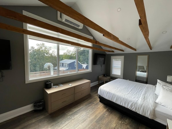 Ein Schlafzimmer mit großem Fenster, Holzbalken, einem Bett, einem Schminktisch und einem Spiegel.