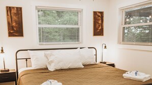 Un dormitorio con cama, mesita de noche, lámpara, ventilador de techo y ventanas.