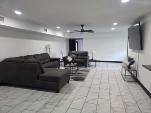 Un salon moderne comprenant un canapĂ© dâangle, un fauteuil inclinable, une table basse et un tĂ©lĂ©viseur fixĂ© au mur.