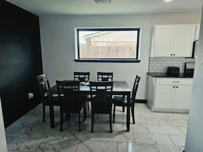 Una cocina compacta con una mesa y sillas, una ventana con vista a una valla de madera, y armarios blancos.