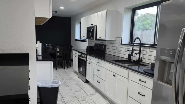 Una cucina moderna con mobili bianchi, un frigorifero in acciaio inossidabile e un pavimento piastrellato.
