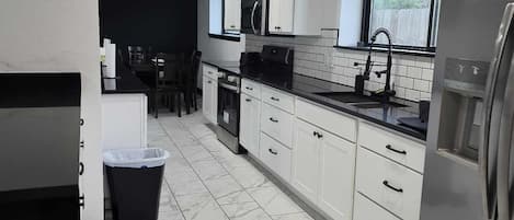 Una cocina moderna con armarios blancos, un refrigerador de acero inoxidable y piso de baldosas.