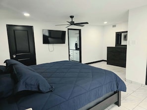 Un dormitorio con cama, ventilador de techo, televisor, armario y espejo.