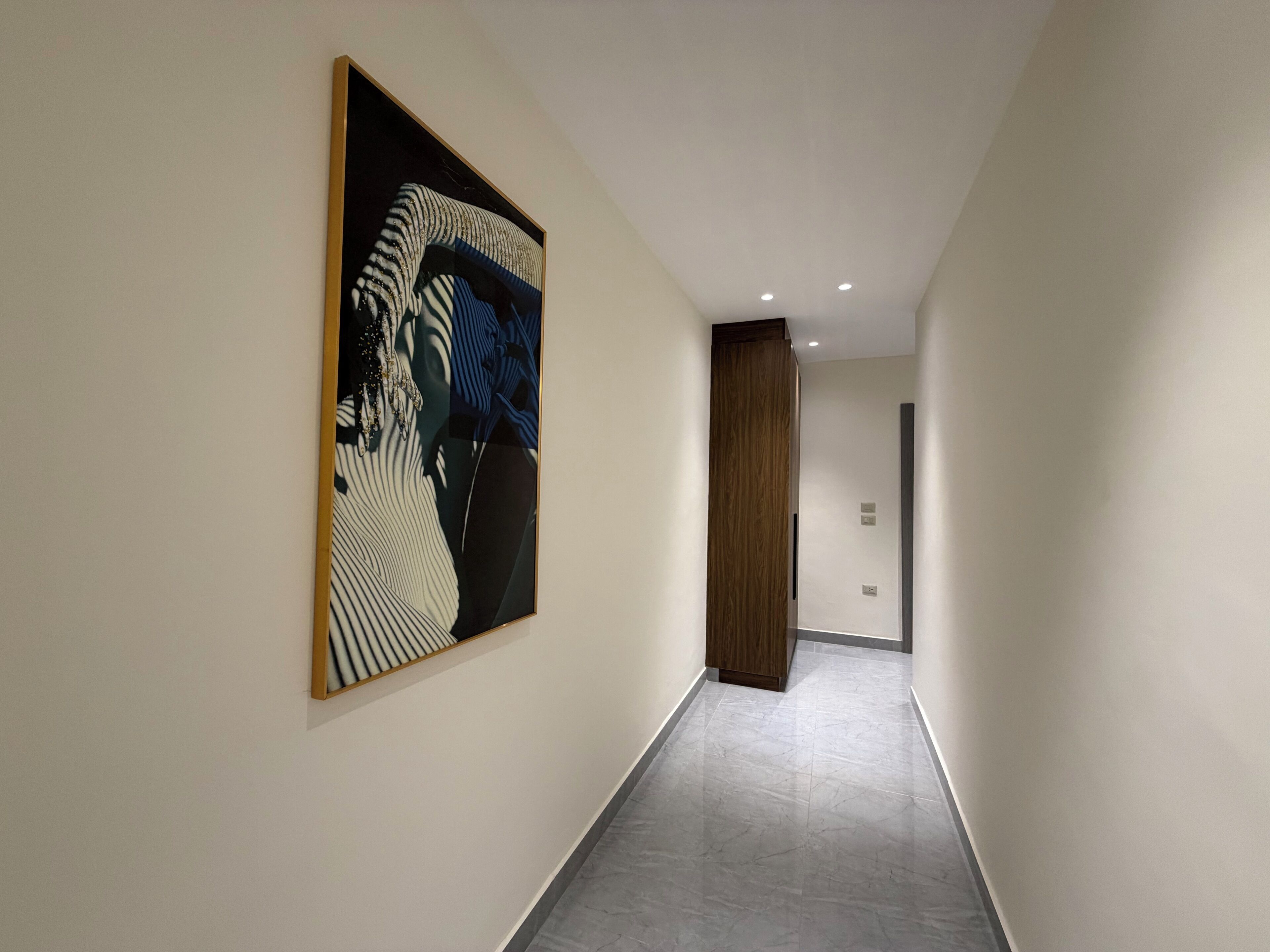 Un corridoio con un'ampia pittura astratta sulla parete sinistra, una porta in legno in fondo e un pavimento piastrellato.