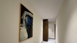 A hallway with a large abstract painting on the left wall, a wooden door at the end, and a tiled floor. - 003jre Apartment With Stunning Boulevar (Amman)