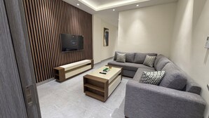 A modern living room with a grey sofa, a wooden TV stand, and a coffee table. - 003jre Apartment With Stunning Boulevar (Amman)