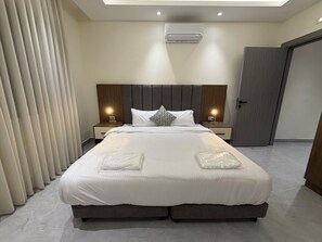 Ein modernes Hotelzimmer mit einem großen Bett, zwei Nachttischen mit Lampen, einer Deckenklimaanlage und einer Tür.