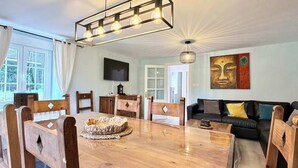 A dining area with a wooden table and chairs, a sofa, and a television on the wall. - The Cliffs - Casa Cadaval (Ortigueira)