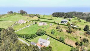 An aerial view of a rural property with multiple buildings, green fields, and a coastline. - The Cliffs - Casa Cadaval (Ortigueira)