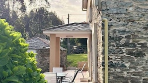 A patio with a table and chairs, a stone wall, and a view of the surrounding landscape. - The Cliffs - Casa Cadaval (Ortigueira)