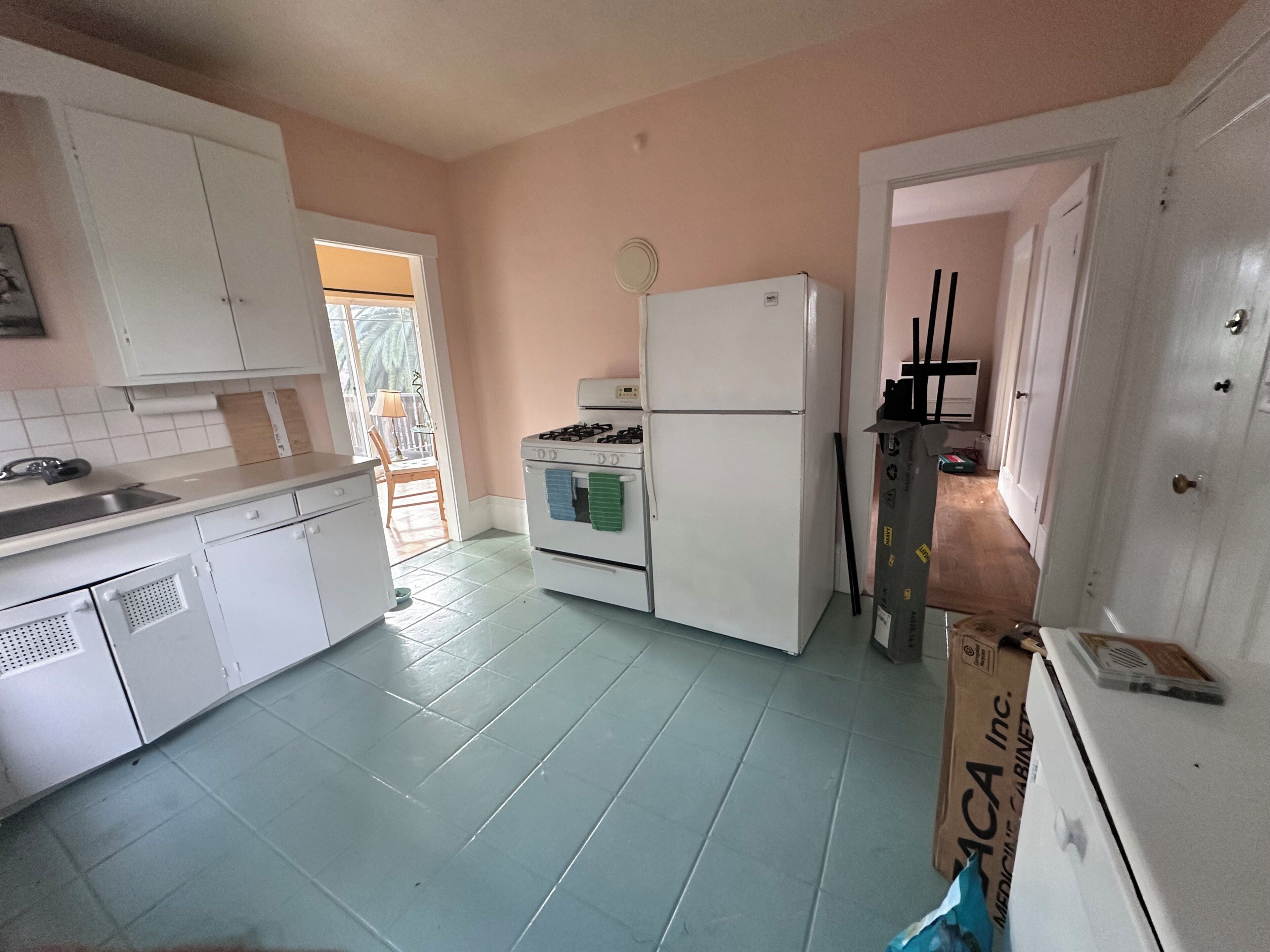 A kitchen with white cabinets, a stove, a refrigerator, and a door leading to another room.