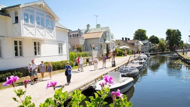 En strandpromenad längs kanalen, med hus, en smal vattenväg och båtar som ligger förtöjda längs sidan.