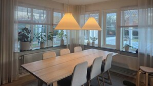 Ett konferensrum med ett långt bord, stolar, krukväxter och stora fönster med persienner.
