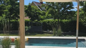 Ett trädäck med en pool, en pergola med ett tak och en bänk.