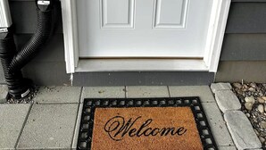 Eine weiße Tür mit Fußmatte, auf der 'Welcome' steht.