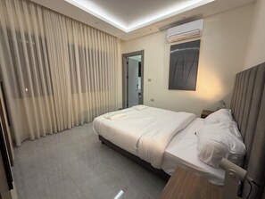 Ein Hotelzimmer mit Bett, Vorhängen, einer Klimaanlage, einem Nachttisch und einem Wandbild.