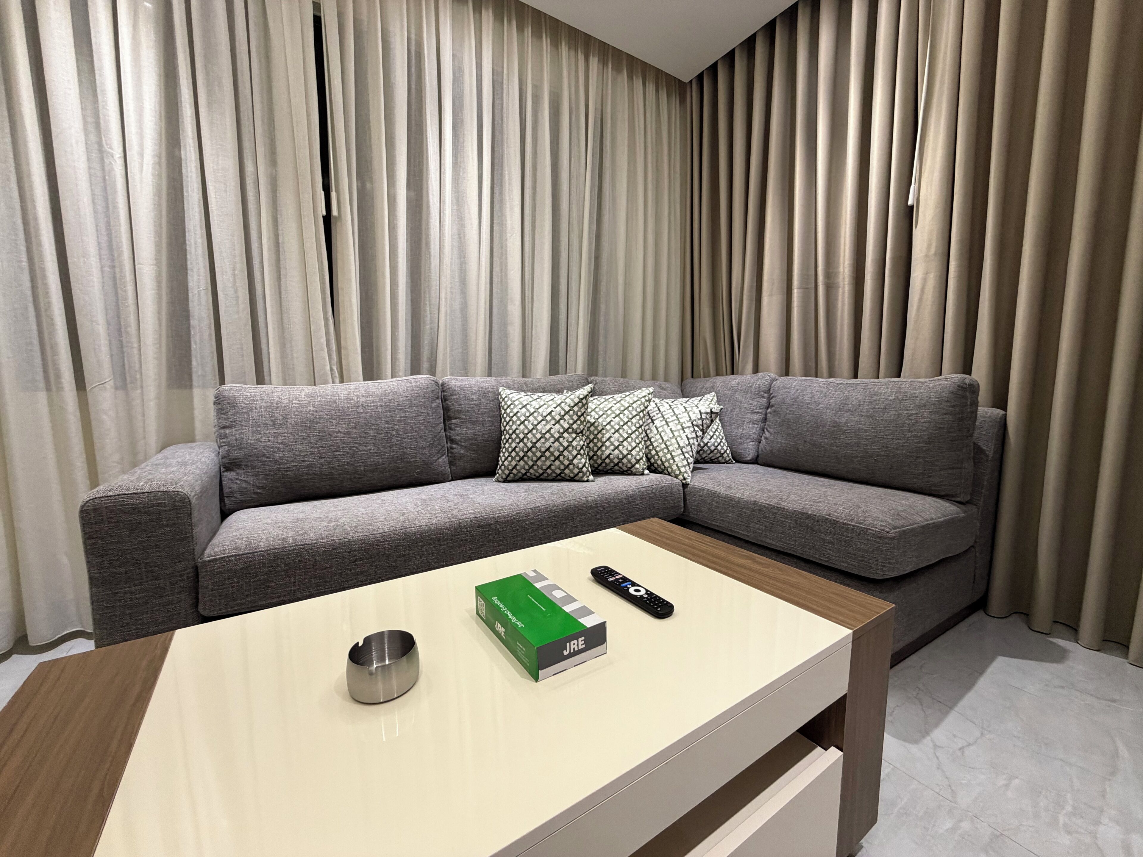 A modern living room with a grey sectional sofa, a wooden coffee table, and a remote control.