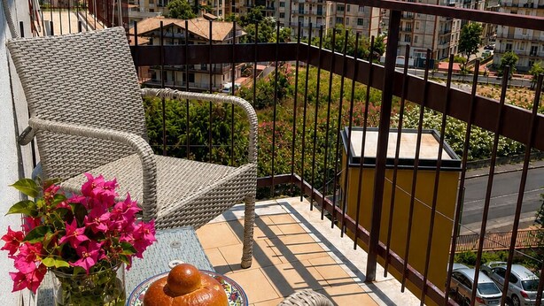 A balcony with wicker chairs, a table with food and drinks, and a view of a residential area. - Room with private bathroom in apartment near policlinico cittadella catania (Gravina di Catania)