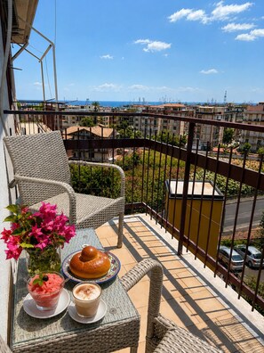A balcony with wicker chairs, a table with food and drinks, and a view of a residential area.