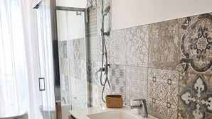 A modern bathroom with a glass shower enclosure, a wooden vanity, and patterned tiles. - Room with private bathroom in apartment near policlinico cittadella catania (Gravina di Catania)