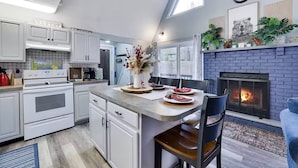 Een moderne keuken met witte kasten, een centraal eiland, een open haard en een eethoek met uitzicht op de omgeving.