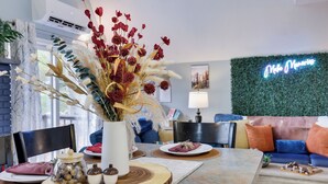 Een moderne woonkamer met een bank, een eettafel met een bloemenvaas, en een neonbord aan de muur.
