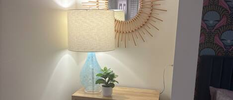 A corner room with a wooden cabinet, a mirror with a sunburst design, a lamp, and a potted plant.