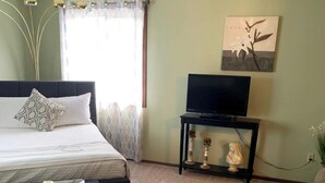Une chambre à coucher avec un lit, un téléviseur posé sur un meuble, une petite table avec une bougie et un vase rempli de fleurs.