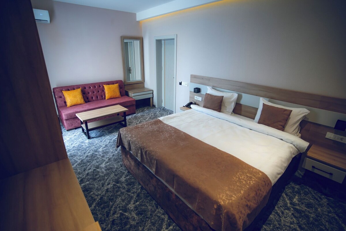 Een hotelkamer met een bed, een slaapbank, een nachtkastje, een spiegel en een deur.