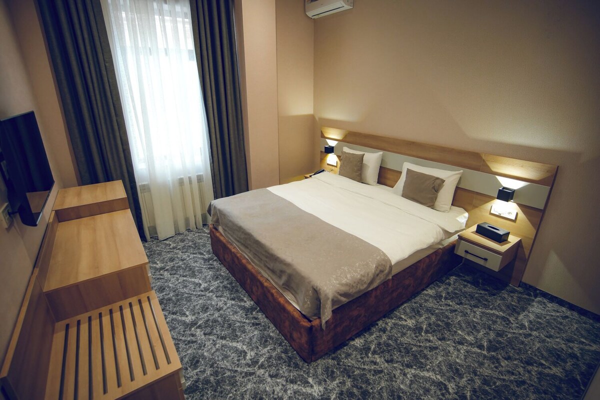 Een hotelkamer met een bed, nachtkastjes, een bureau en een televisie.