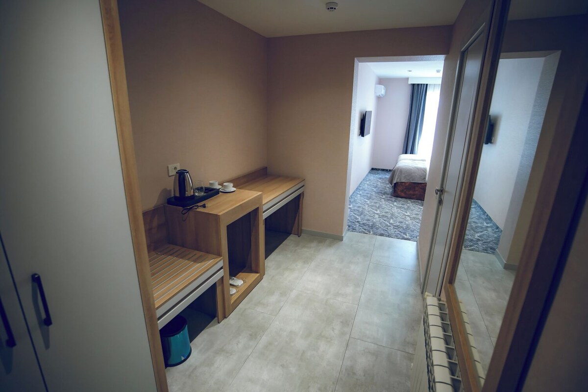 Een hotelkamer met een houten bureau, een klein tafeltje met een waterkoker, een prullenbak en een bed op de achtergrond.