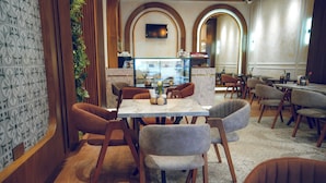 Un restaurant avec une table en marbre, des chaises en bois et un mur recouvert de carreaux décorés d’un motif floral.