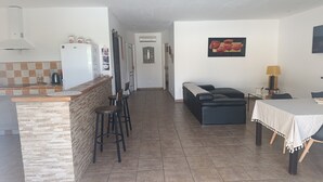 Eine Küche mit Kühlschrank, Kaffeemaschine und einer Wandfliesenverkleidung. Es gibt einen Essbereich mit Tisch, Stühlen und einer Couch.
