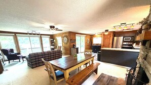 A cozy cabin interior with a dining area, kitchen, and living room. - Lakefront Rustic 4-Bedroom House with Private Dock (Lake Ozark)