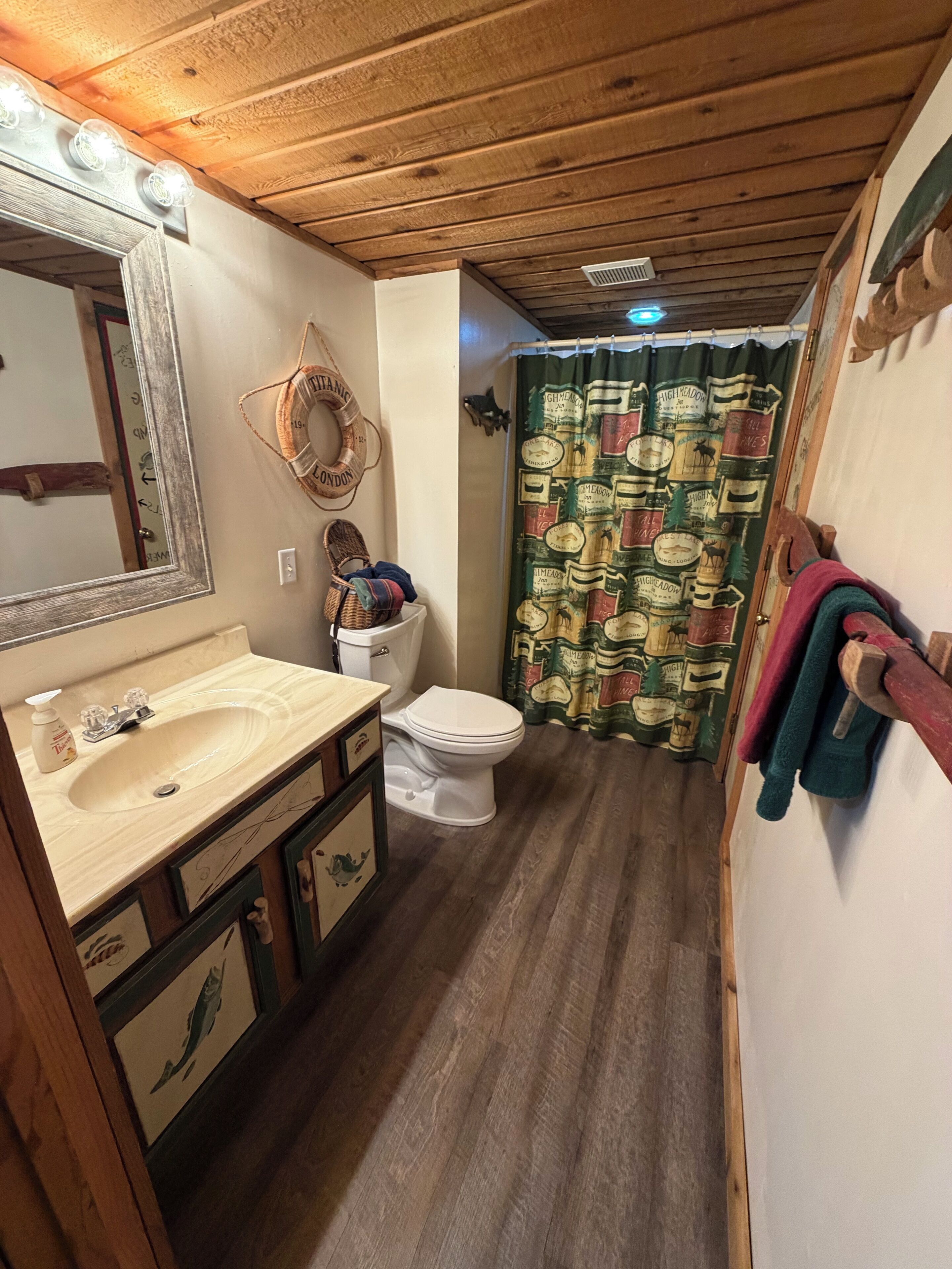 A bathroom with a wooden ceiling, a sink with a mirror, a toilet, and a shower curtain with a vintage pattern.