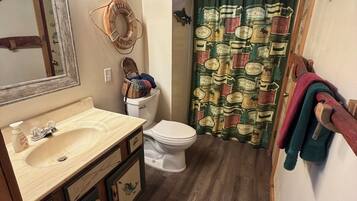 A bathroom with a wooden ceiling, a sink with a mirror, a toilet, and a shower curtain with a vintage pattern.