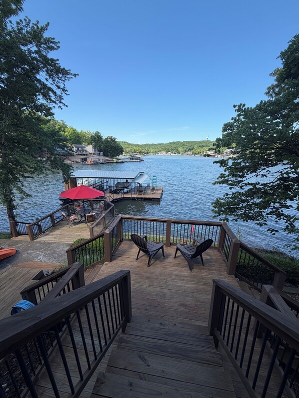 A wooden deck with chairs and a table, overlooking a lake with docks and boats.